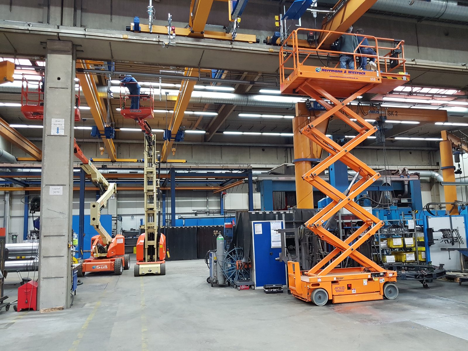 Kranprüfung in einer Industriehalle mit Hubarbeitsbühnen verschiedener Bauarten und ABUS-Brückenkranen